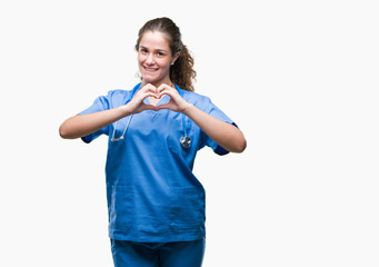 Sticker - Young brunette doctor girl wearing nurse or surgeon uniform over isolated background smiling in love showing heart symbol and shape with hands. Romantic concept.