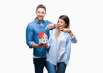 Sticker - Young couple in love holding house over isolated background very happy pointing with hand and finger