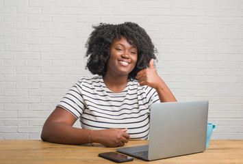 Canvas Print - Young african american woman sitting on the table using computer laptop happy with big smile doing ok sign, thumb up with fingers, excellent sign