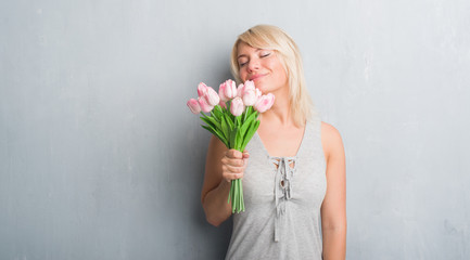 Poster - Caucasian adult woman over grey grunge wall holding pink flowers with a confident expression on smart face thinking serious