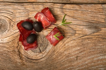 closeup of thin slices of prosciutto with olives on wooden board