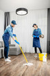 © rh2010 - Professional cleaners in blue uniform washing floor and wiping dust from the furniture in the living room of the apartment. Cleaning service concept