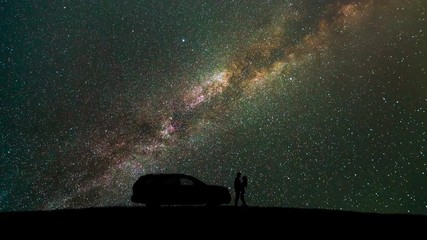 Wall Mural - The man and woman standing near a car against the starry sky. time lapse