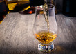 Pouring single malt scotch whisky into whisky glass on wooden table