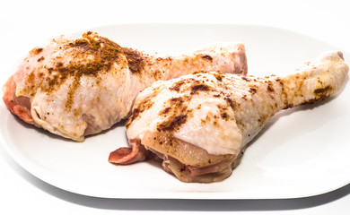 Two chicken legs with spices on a white plate, cooking concept