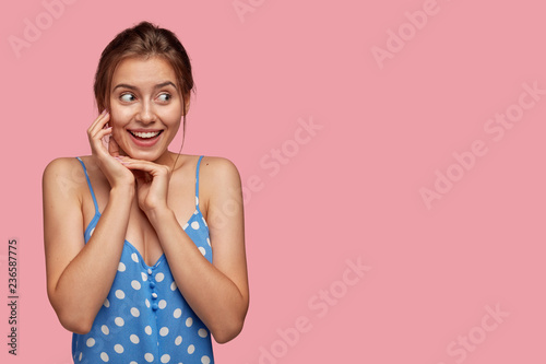 Fotografie, Obraz Cute emotive glad woman with toothy smile, keeps hands near face, looks with hap