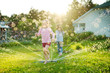 © MNStudio - Adorable little girls playing with a sprinkler in a backyard on sunny summer day. Cute children having fun with water outdoors.