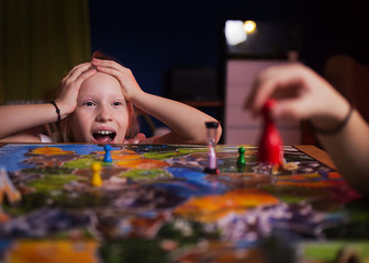 Wall Mural - Board game concept - your move. Little girl watched the game and shock from the action move. Board game field, many figures. Kid girl play in board game at home on dark blurred background