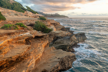 Wall Mural - Waves Breaking into Makawehi Bluff while warm sunrise light illuminates the clouds, Kauai, Hawaii