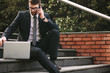 © Jacob Lund - Businessman sitting on steps with laptop talking over phone