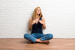 © luismolinero - Blonde girl sitting on the floor proud and self-satisfied in love yourself concept on white brick wall background