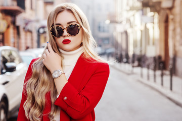 Wall Mural - Outdoor fashion portrait of young beautiful fashionable lady wearing stylish turtle frame sunglasses, luxury wrist watch, white turtleneck, red blazer, posing in street of european city. Copy space
