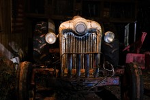 An Operational Antique Or Vintage Tractor In An Old Dimly Lit Barn. Angle Gives The Tractor An Evil Or Mean Appearance.