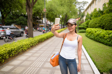 Young beautiful Asian tourist woman taking selfie with mobile phone