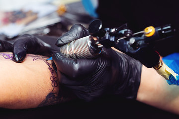 Wall Mural - Close up of the tattoo artist hands creating a tattoo on a girl's arm