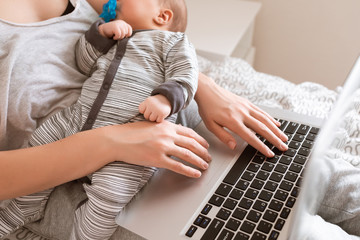 Busy young woman working or study on laptop computer while holding her baby in arms at home