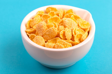 Crispy corn flakes in clay bowl on bright blue background