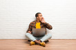 © luismolinero - African american man sitting on the floor with his laptop shouting with mouth wide open to the lateral
