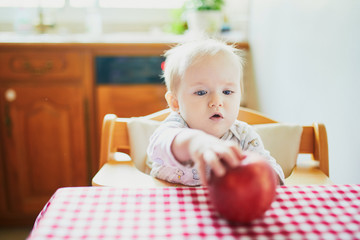 Wall Mural - Cute baby girl eating apple in the kitchen