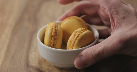 Wall Mural - man hand put orange macarons in white bowl on wood table