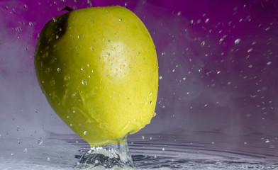 Wall Mural - Green apple and splashes of water on a colored background