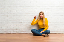 Young Girl Sitting On The Floor Showing And Lifting A Finger In Sign Of The Best