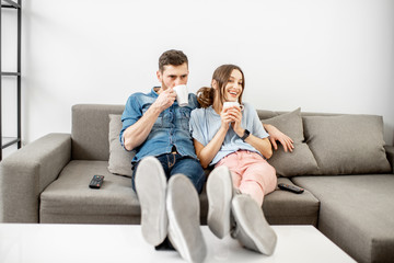 Young couple dressed casually sitting together on the couch and watching TV at home