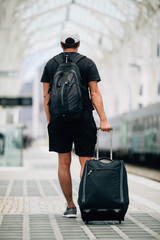 Full length portrait of a happy young man walking with suitcase at train station. Travel concept.