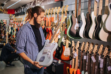 Young Bearded Musician Hold Light-blue Electric Guitar In Hands. He Looks At It.