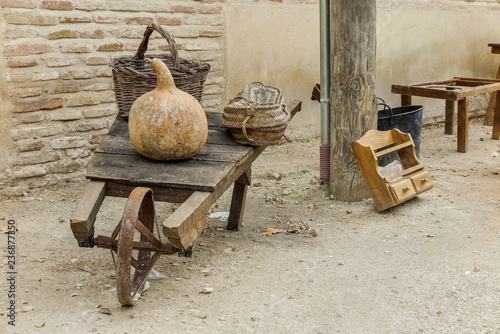 Fotografía antique wooden wheelbarrow with iron wheel carrying a pumpkin and wicker baskets