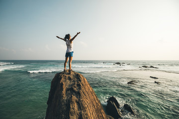 successful young woman outstretched arms on seaside rock cliff edge