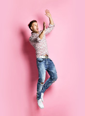 Excited young man in popular shirt jumping celebrating success pointing hands up over pink