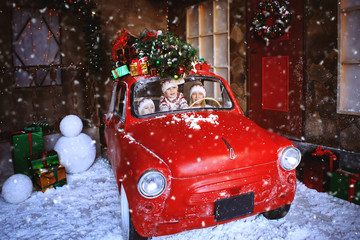 Wall Mural - Two brothers in knitted sweaters with deer sit in a red Christmas car and rejoice at the advent of Christmas.