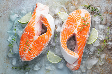 Two raw fresh salmon or trout steaks on ice, rich in omega-3 oil, with lime, thyme and olive oil on a blue rusty background. Healthy and diet food. Top view. Flat lay