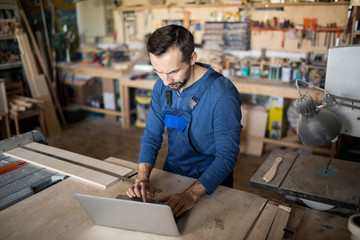 High angle portrait of mature carpenter using laptop while working in joinery, copy space