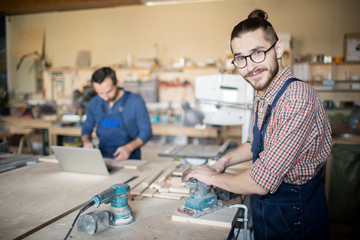 Waist up portrait of modern carpenter sanding wood in workshop and looking at camera, copy space