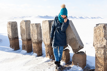 Wall Mural - The concept of livestyle  outdoor in winter. A young woman student in a blue knitting hat and  coat  smiles, heats up and walks through the winter mountains