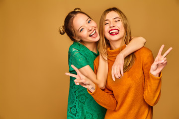 Wall Mural - Two young beautiful blond smiling hipster girls posing in trendy summer clothes. Carefree women isolated on golden background. Positive models going crazy and hugging