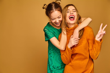 Wall Mural - Two young beautiful blond smiling hipster girls posing in trendy summer clothes. Carefree women isolated on golden background. Positive models going crazy and hugging