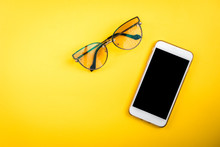 Mobile phone and glasses on yellow background