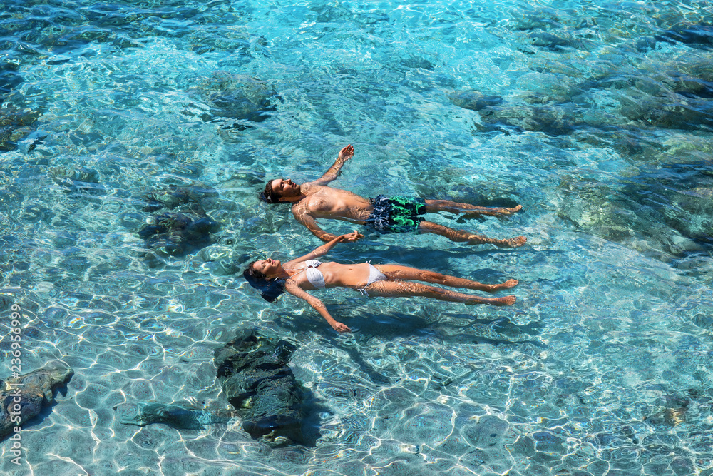 Happy couple swimming in the transparent turquoise sea - obrazy, fototapety, plakaty 