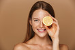 © Drobot Dean - Beauty image of european shirtless woman with long hair holding piece of orange, isolated over beige background