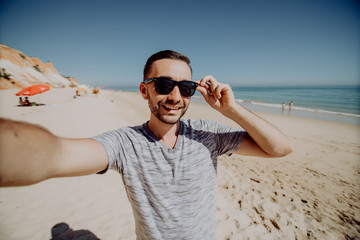 Happy man in sunglasses on vacation laughing at the beach taking selfie