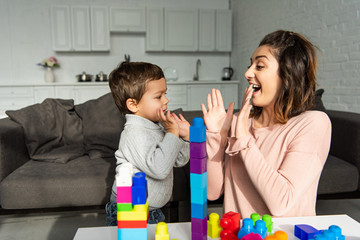 cheerful woman doing pat-a-cake with little son at home