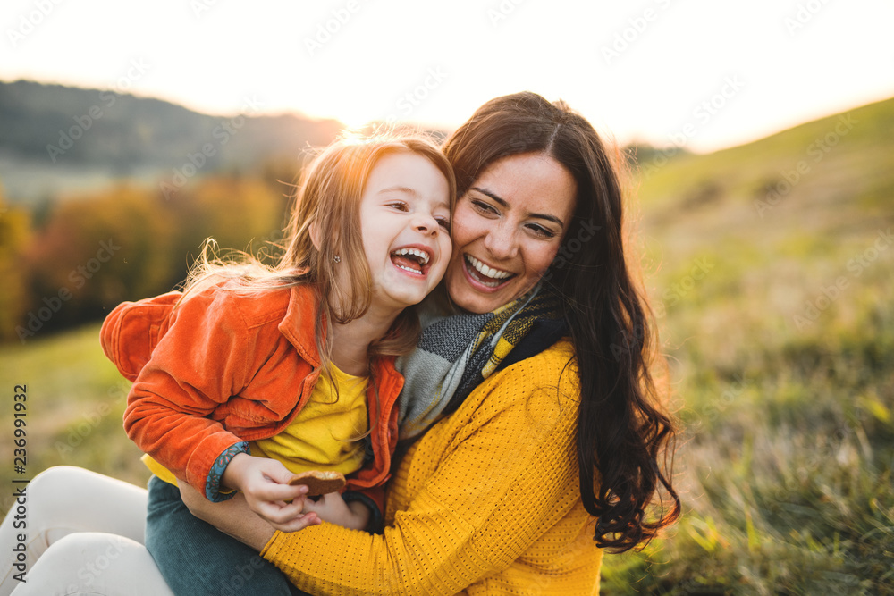 A portrait of young mother with a small daughter in autumn nature at sunset. - obrazy, fototapety, plakaty 