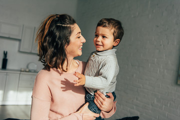 cheerful woman holding adorable little son on hands at home