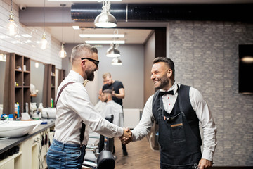 Wall Mural - Hipster man client shaking hands with haidresser and hairstylist in barber shop.