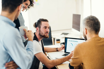 Wall Mural - Group of young businesspeople with laptop working together in a modern office.