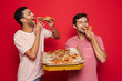 © Drobot Dean - Handsome happy young men friends isolated over red wall background holding big pizza.