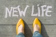 Female feet with text new life written on grey sidewalk